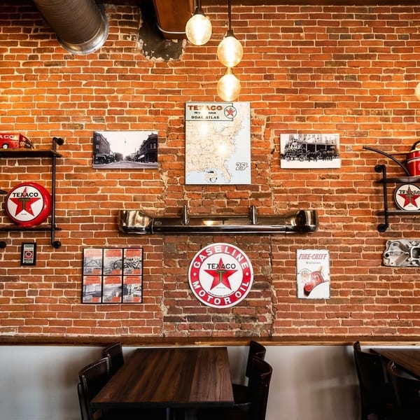 Brick wall decorated with vintage Texaco signs, maps, and automotive memorabilia above dining tables.