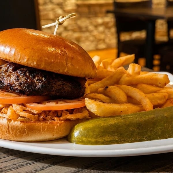 A juicy burger with tomatoes and crispy onions, served with golden fries and a pickle.