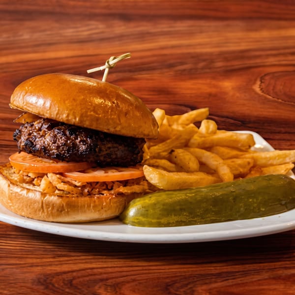 Gourmet burger with fries and a pickle spear on a white plate, on a wooden table.