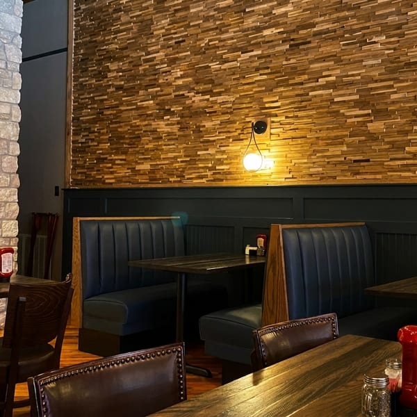 Restaurant interior with stone and wood panel walls, dark booths, and wooden tables with condiments.